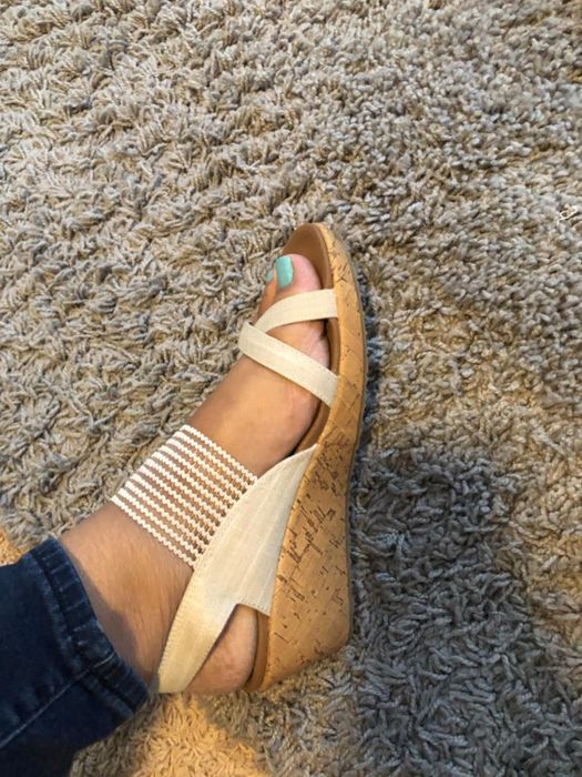A reviewer showcasing cork wedge sandals with cream-colored straps