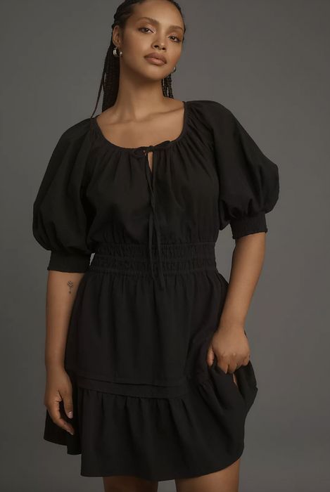 A person confidently poses in a vintage-inspired dress featuring puffed sleeves, set against a simple backdrop
