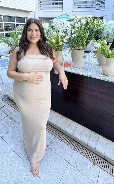 A reviewer wearing a form-fitting sleeveless dress posing next to a vibrant floral arrangement