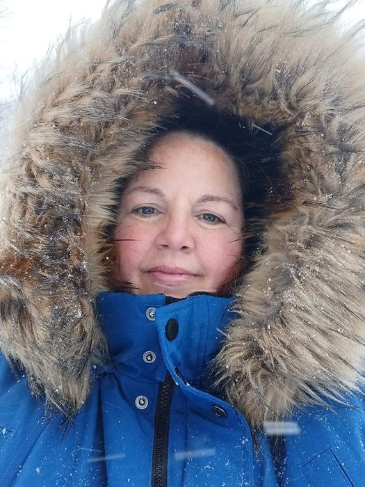 Person wrapped up in a cobalt blue winter coat with a fur-lined hood, standing in snowy weather
