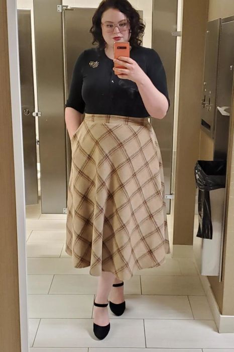 A reviewer taking a mirror selfie wearing the tan skirt with a black shirt tucked in