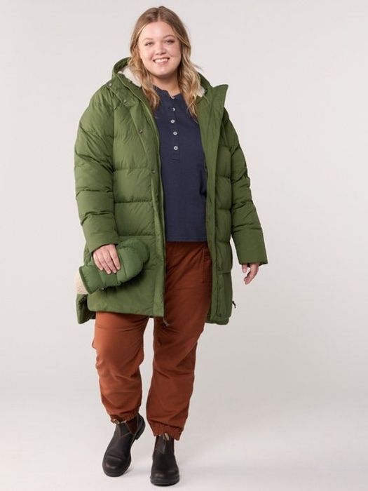 A person models a long green puffer coat with casual pants and boots, accessorized with a matching scarf, possibly for a winter fashion article.
