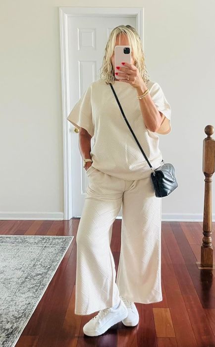 A reviewer takes a selfie in a home mirror, wearing a matching relaxed-fit top and wide-leg pants, accessorized with a crossbody bag and sneakers