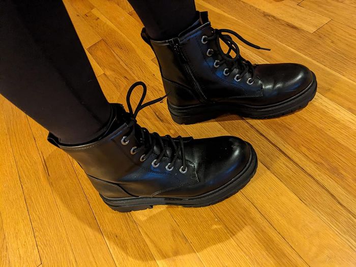 A person wearing black lace-up combat boots on a wooden floor
