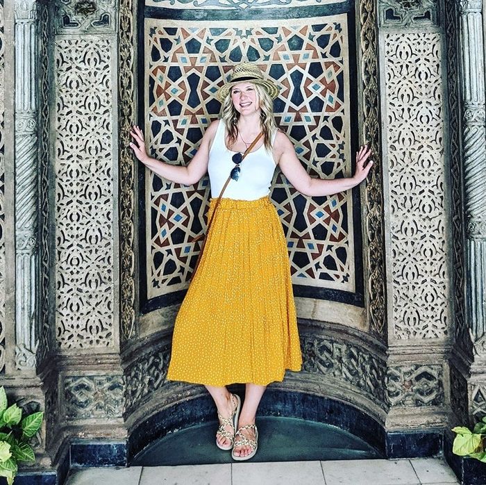 A reviewer wearing the same high-waisted pleated midi skirt in mustard yellow