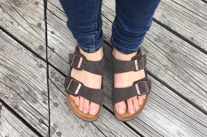 A person showcasing dark brown Birkenstock sandals featuring two adjustable buckles