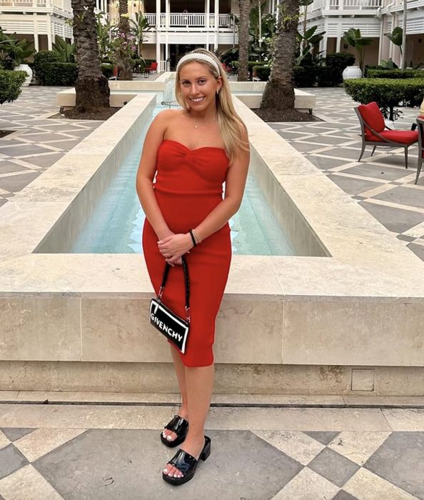 A reviewer poses by a pool in a strapless red dress, accessorized with a Givenchy bag