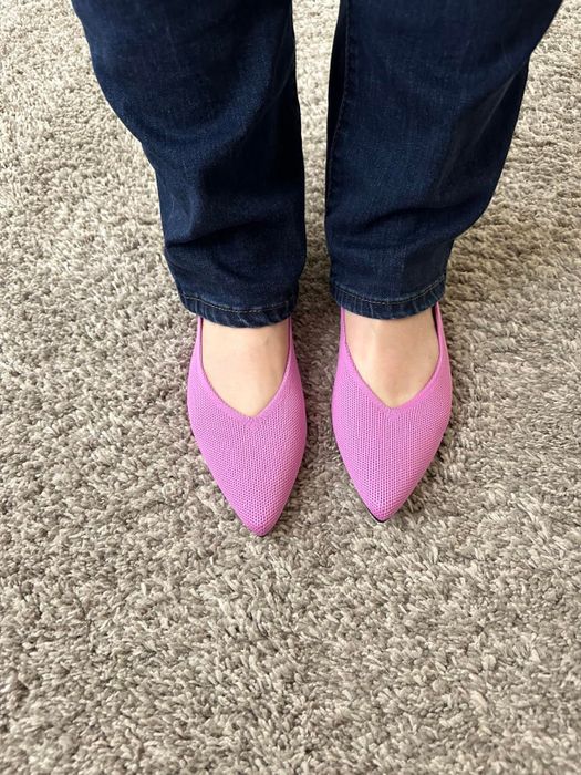 A reviewer wearing chic pink pointed-toe flats with a modern design
