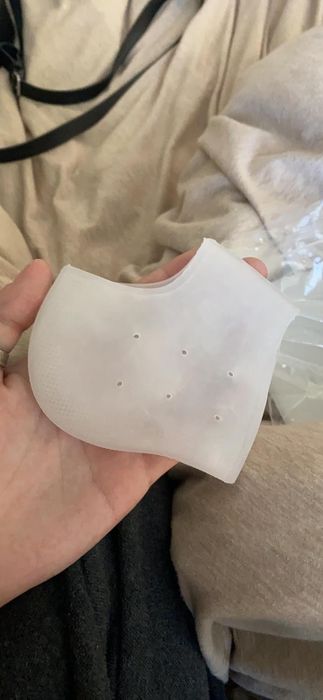 A hand holds a folded white face mask with small holes in it, against a fabric background