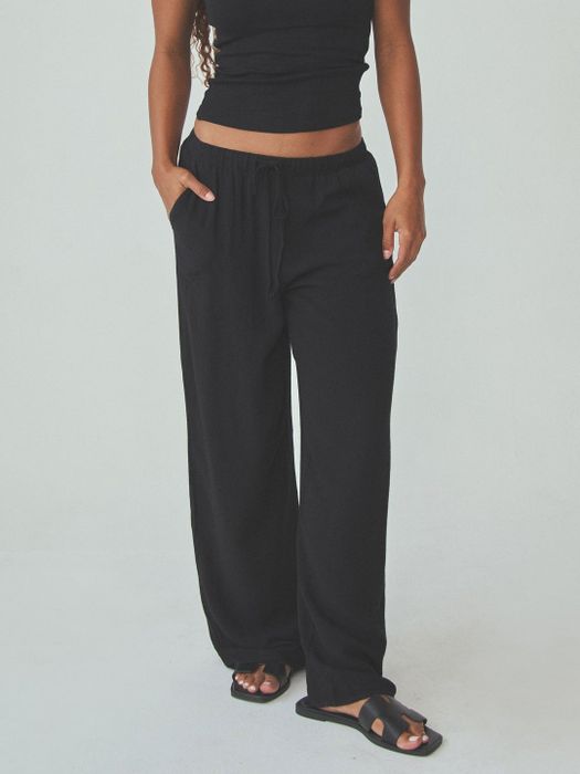 A person modeling relaxed, loose-fit pants featuring a drawstring waist, paired with sandals. The outfit exudes a casual, laid-back vibe perfect for shopping