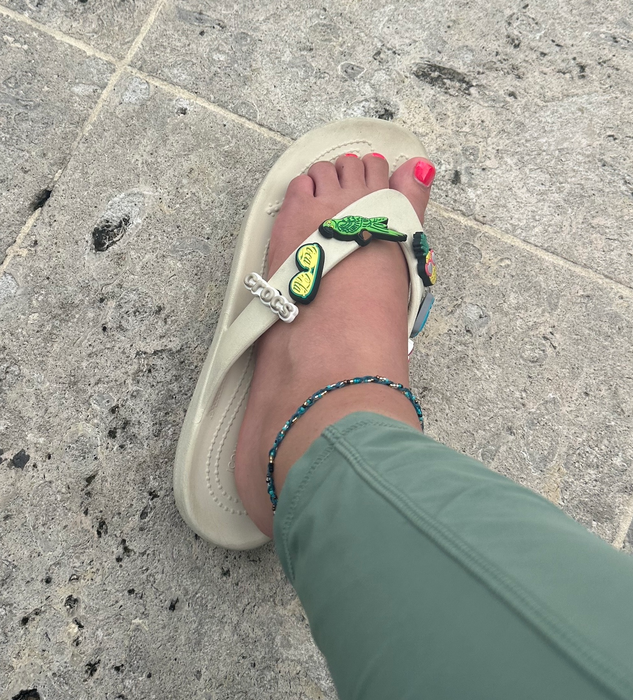 The author showcasing white Crocs sandals adorned with a parrot charm