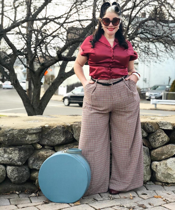 A reviewer wearing the brown plaid pants paired with a red top