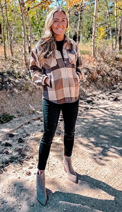 a reviewer showcasing the shacket in brown and cream, worn buttoned up with black jeans
