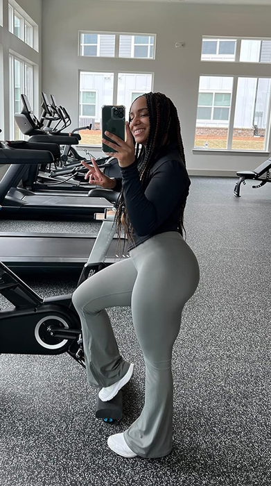 A gym-goer in workout attire snapping a selfie inside a fitness center equipped with treadmills and exercise bikes