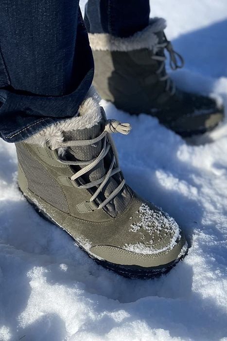 A reviewer wearing gray winter boots and jeans, standing in the snow.