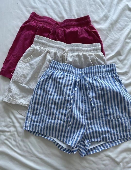 Three pairs of shorts—red, white, and blue-striped—are neatly laid out on a bed