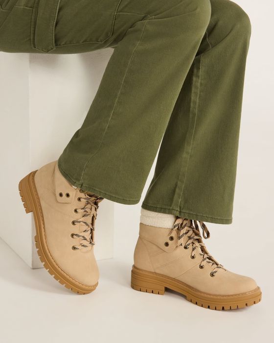 A person wearing tan hiking boots with green pants, sitting on a white block