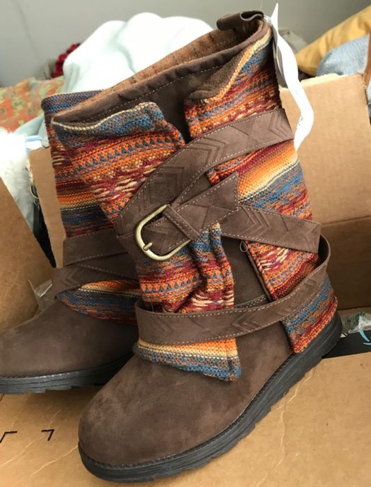 A reviewer’s photo of chic ankle boots featuring multicolored woven straps and a buckle, elegantly placed atop a cardboard box.