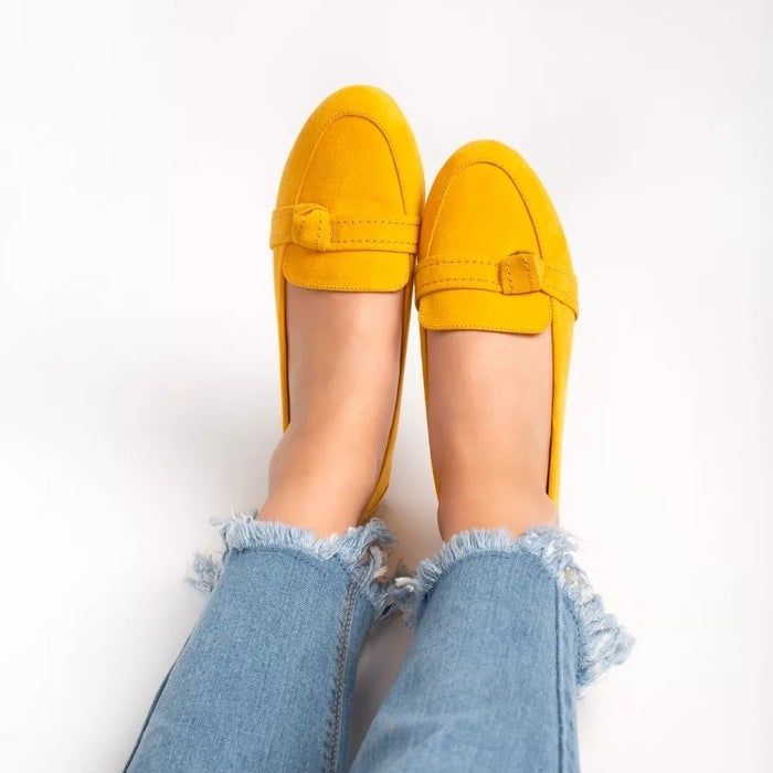 Individual sporting yellow loafers featuring a buckle design paired with distressed jeans. Image used in a shopping feature