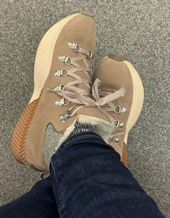 A reviewer wearing tan hiking boots with thick soles, with their legs crossed over denim on a textured surface.