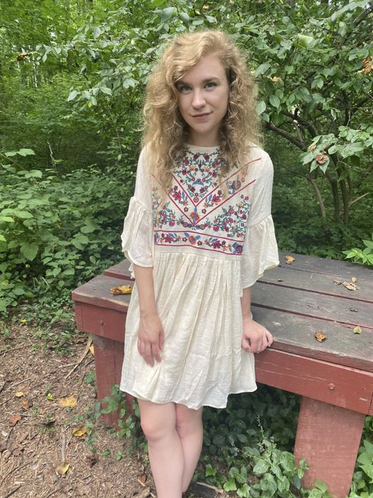 A Mytour editor in a white dress featuring an embroidered floral pattern on the chest.