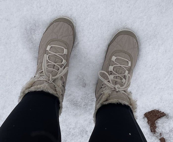 A person standing in the snow wearing quilted boots with a fur trim.