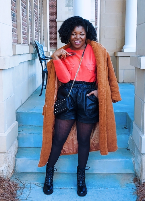 reviewer styling black shorts with tights, a cozy sweater, and a long coat