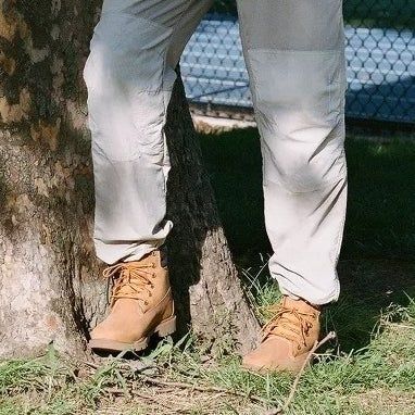 A model wearing tan Timberland boots and light-colored pants, leaning casually against a tree