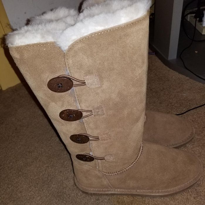 A photo of tall suede boots with plush lining and side button closures, elegantly displayed on a carpeted floor.