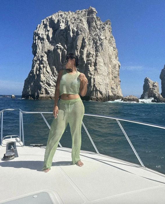 A reviewer in a net two-piece outfit poses on a boat with a dramatic rock formation in the background