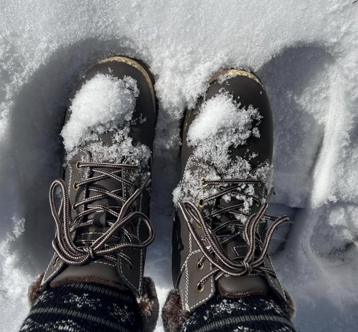 Two boots covered in snow, resting on a snowy surface, with striped socks peeking out above the boots.