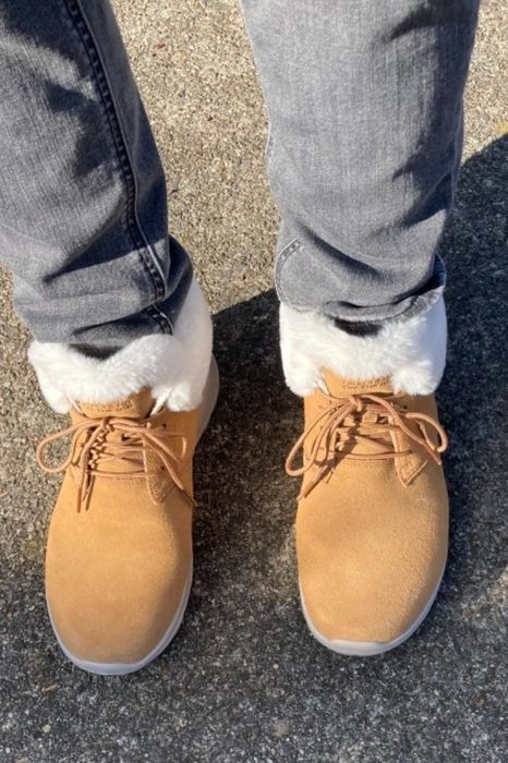 A reviewer wearing light jeans and tan boots with fluffy white lining, standing on a concrete surface.