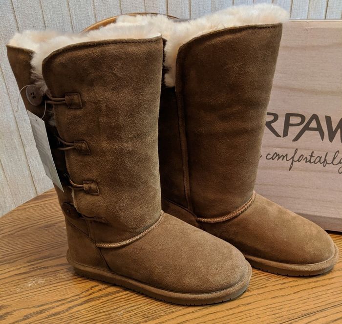 Another image of brown suede winter boots with fur lining and button accents, resting on a wooden table with a box in the background.