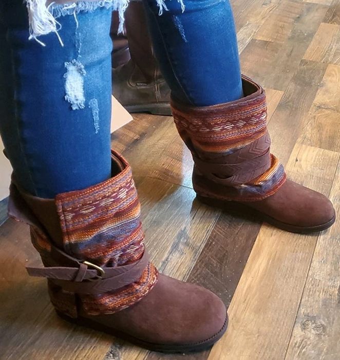 A reviewer styled in distressed jeans and patterned wrap-around boots, standing on a wooden floor, showing off a fashionable look.