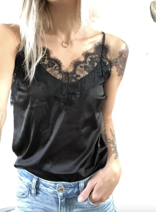 A person wearing a black satin camisole with lace trim, paired with light denim jeans