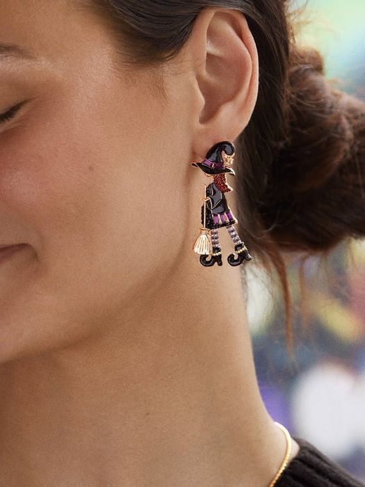 Close-up of someone wearing Halloween earrings featuring a witch on a broomstick