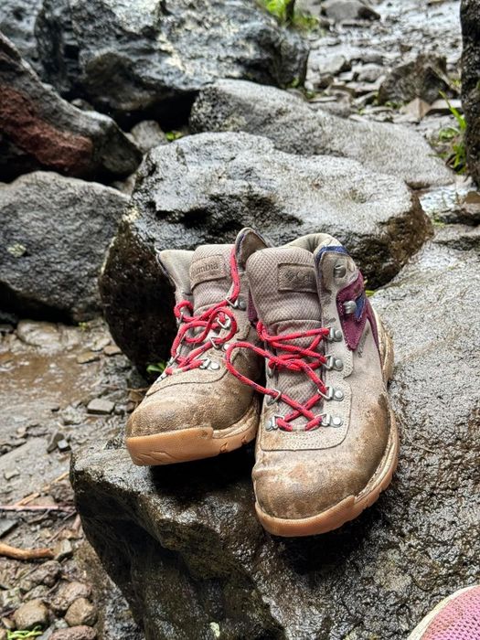 Hiking boots with red laces positioned on a damp, rocky trail.