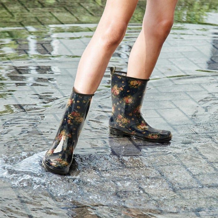 An individual stepping through a puddle on a paved path while wearing floral-patterned rain boots