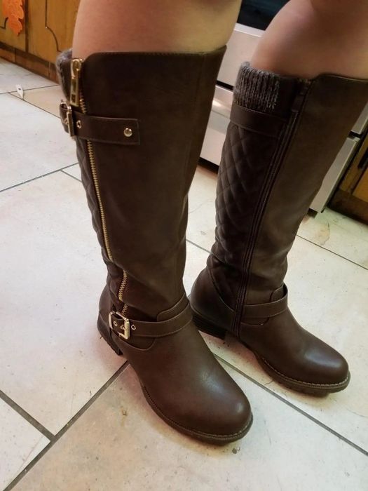 A reviewer is wearing a pair of brown knee-high boots.