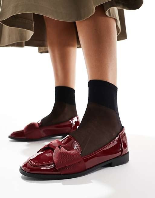 Person wearing black sheer socks and shiny red bow loafers, matched with a flowy skirt
