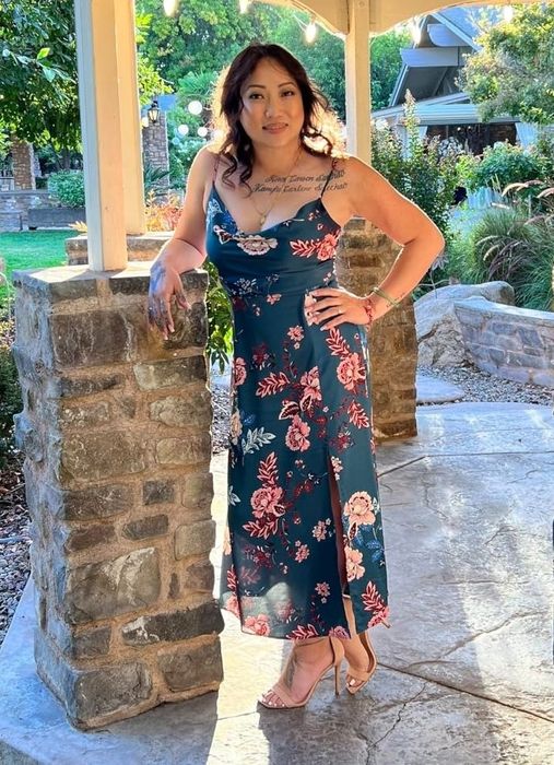 A reviewer in a floral dress stands beneath a gazebo, surrounded by lush garden scenery.