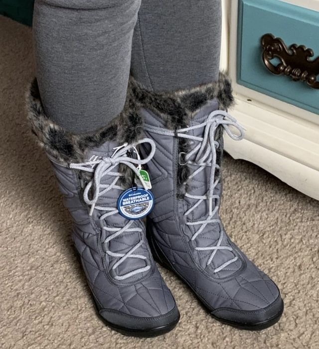 A person in grey quilted winter boots with fur trim, standing on a carpet.