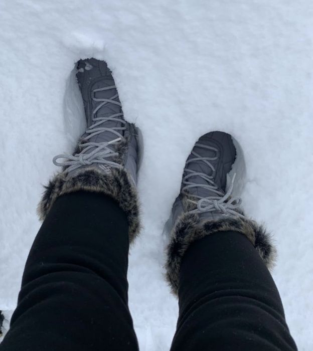A person wearing fur-lined winter boots, standing on snow.