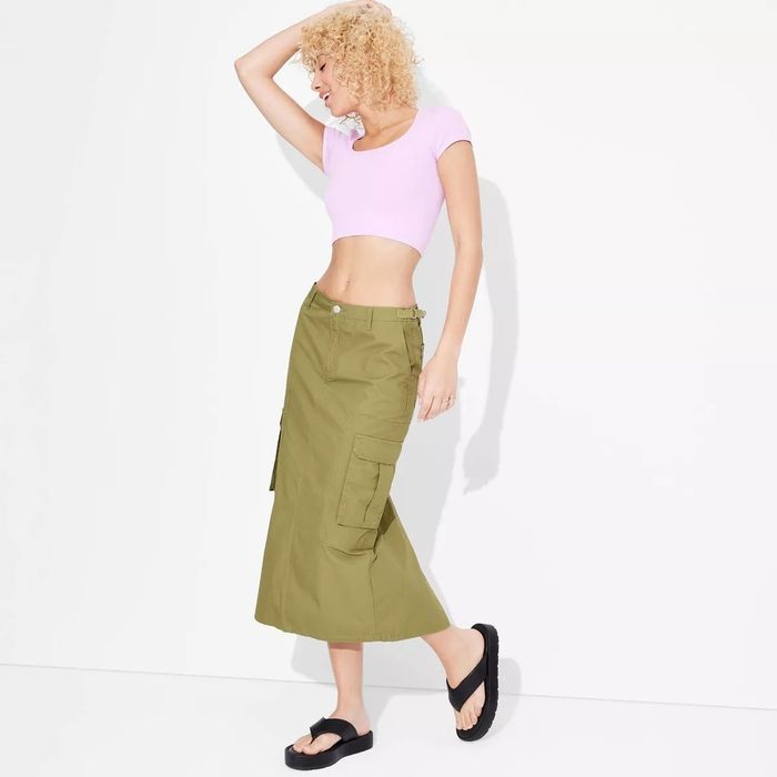 A model posing in a pink crop top and olive green cargo skirt, exuding casual, trendy style