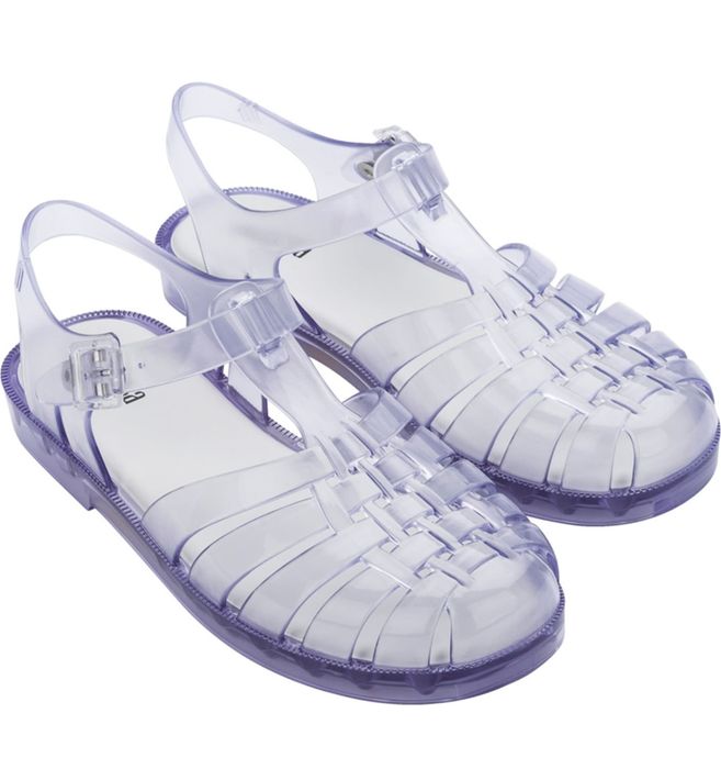 Clear plastic jelly sandals featuring a closed-toe design and an ankle strap with a buckle. The sandals have a woven pattern on top and flat soles.