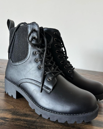 A pair of black combat boots with lace-up fronts and elastic side panels, showcased on a wooden surface.