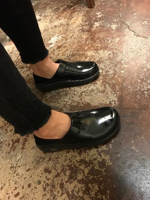 A reviewer wearing shiny black clogs