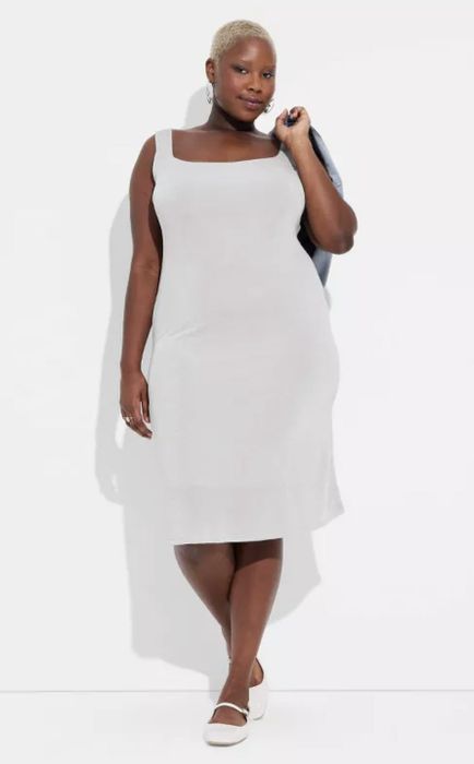 A model shows off a sleeveless white dress paired with white shoes and a denim jacket draped over one shoulder