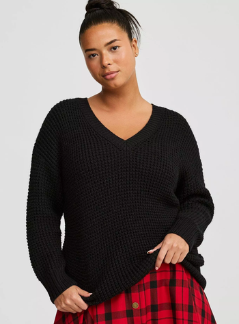 A model wearing a cozy knit sweater paired with a red plaid skirt.