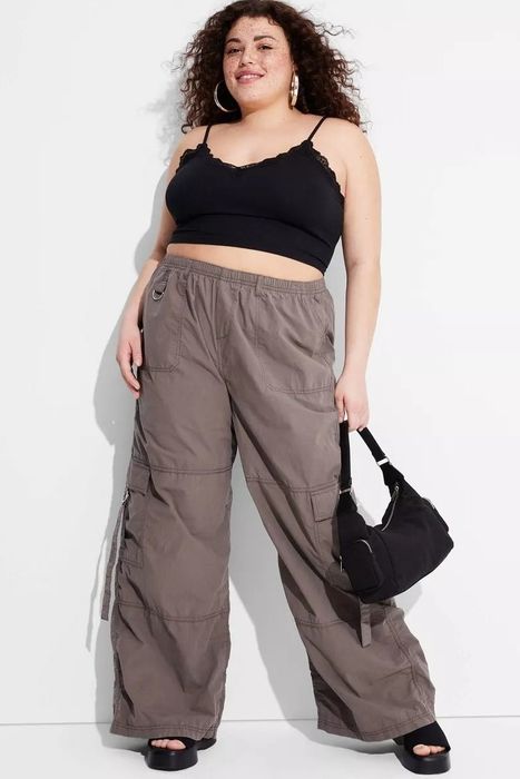 A model dressed in brown cargo pants, a black crop top, and carrying a black handbag
